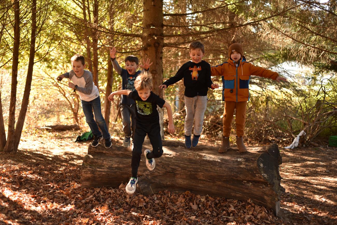 Elementary boys playing outside, jumping off a log